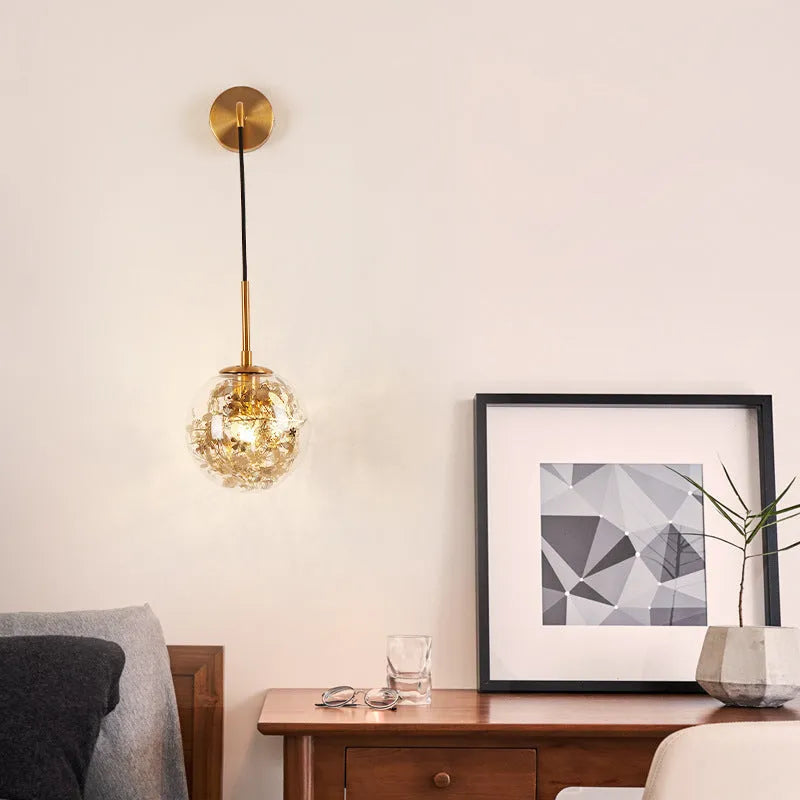 Modern small glass wall lamp in golden flower finish mounted on a bedroom wall.