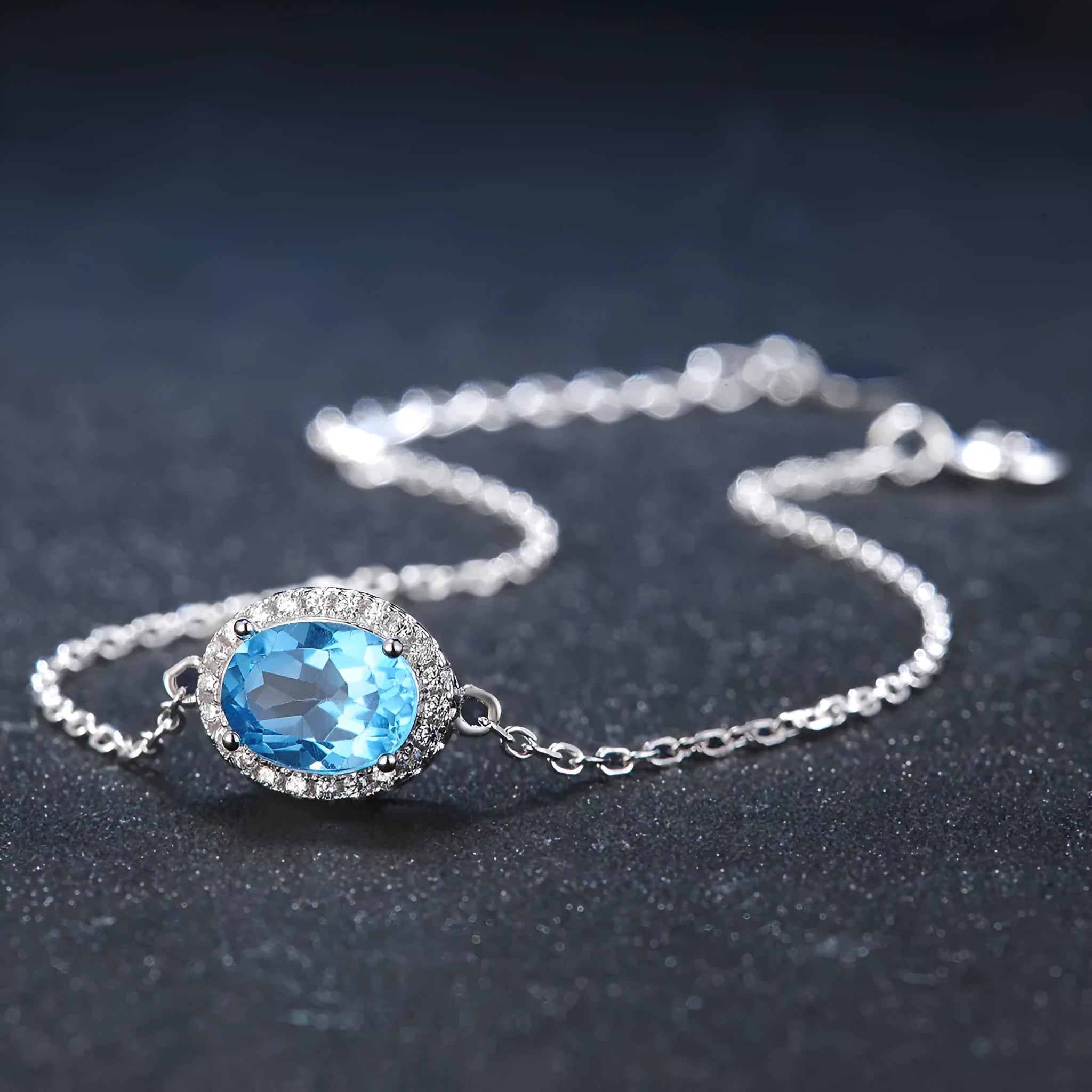 Four-piece sterling silver jewellery set with blue topaz gems: earrings, ring, pendant, and necklace on a geometry pattern.