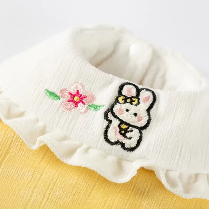 Small dog wearing a lavender bunny embroidered pet coat with white ruffled collar and fluffy pom-pom tail