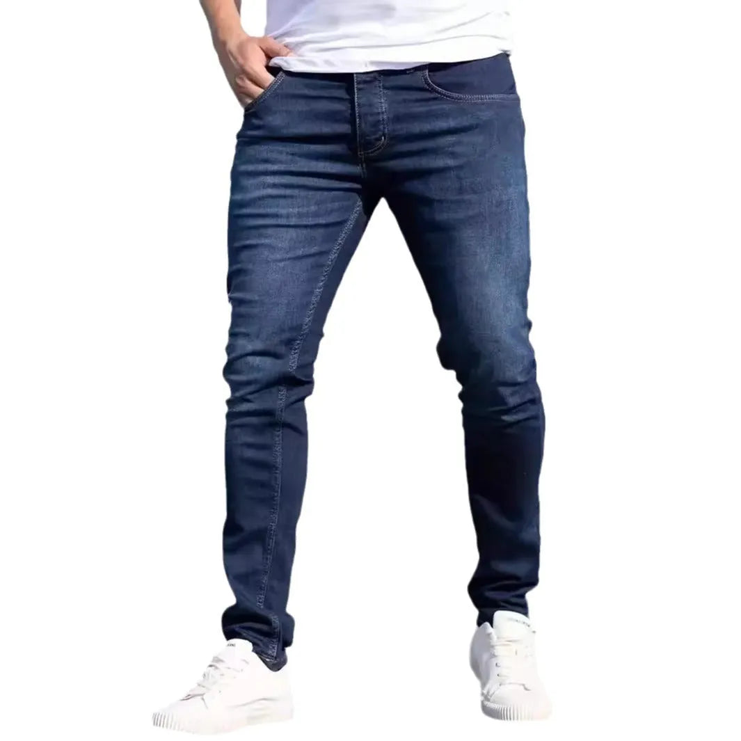 Men's dark blue skinny fit cotton jeans with a mid-rise waist and zipper fly on a plain background.