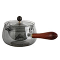 Grey and transparent rotary glass teapot with wooden handle and infuser on a kitchen counter