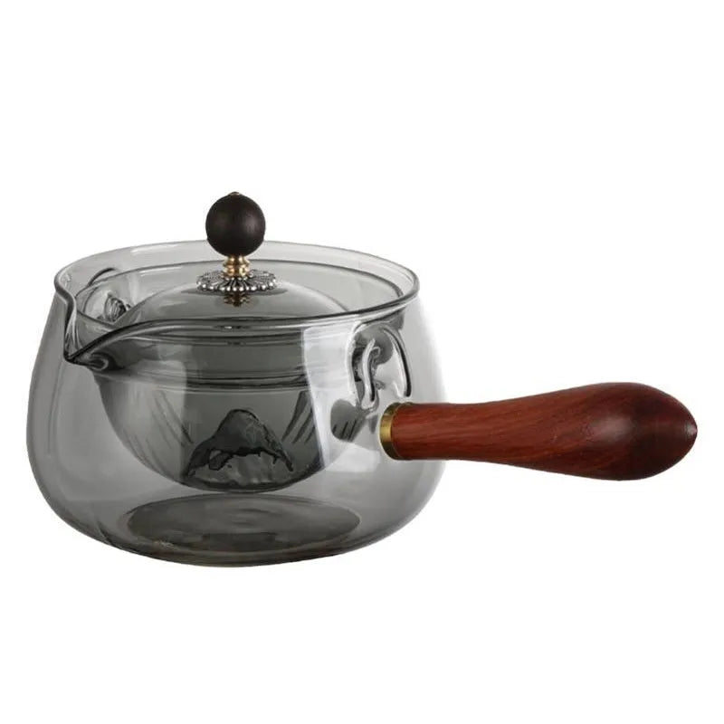 Grey and transparent rotary glass teapot with wooden handle and infuser on a kitchen counter