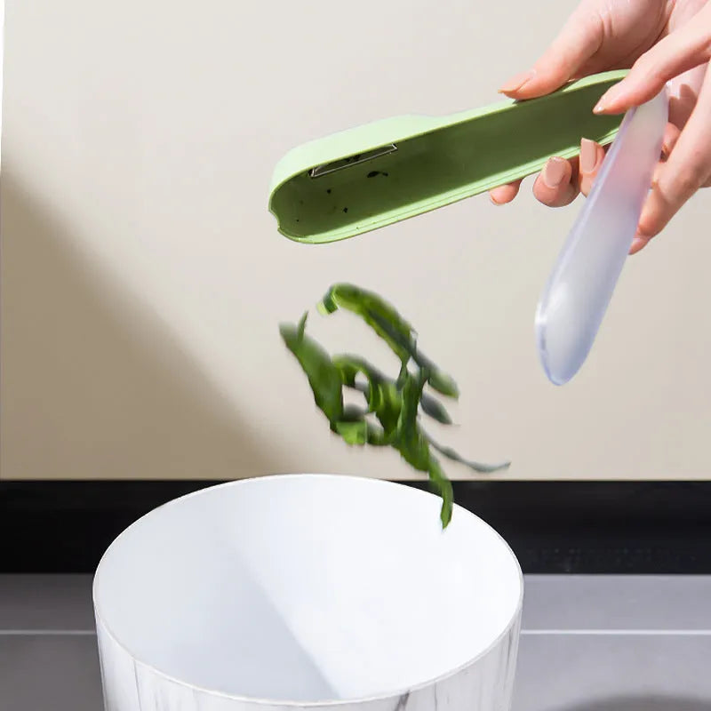 Dark green kitchen peeler with storage tube and stainless steel blade on a kitchen counter.
