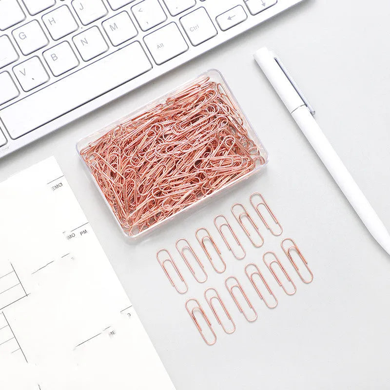 100 rose gold coloured heart-shaped metal paper clips in a box.