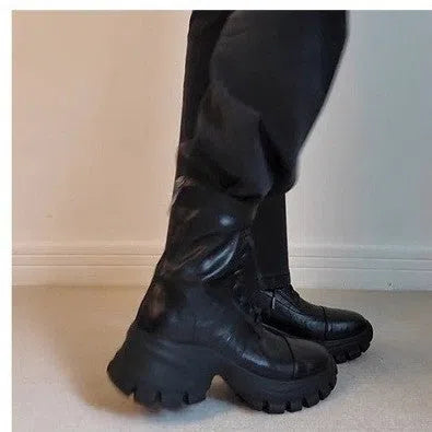 Black thick-soled motorcycle boots with back zipper, lace-up front, round toe, and rubber sole on a neutral background