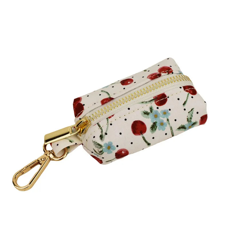 Red cherry print pet collar, lead, and harness set with light gold buckles and matching waste bag dispenser