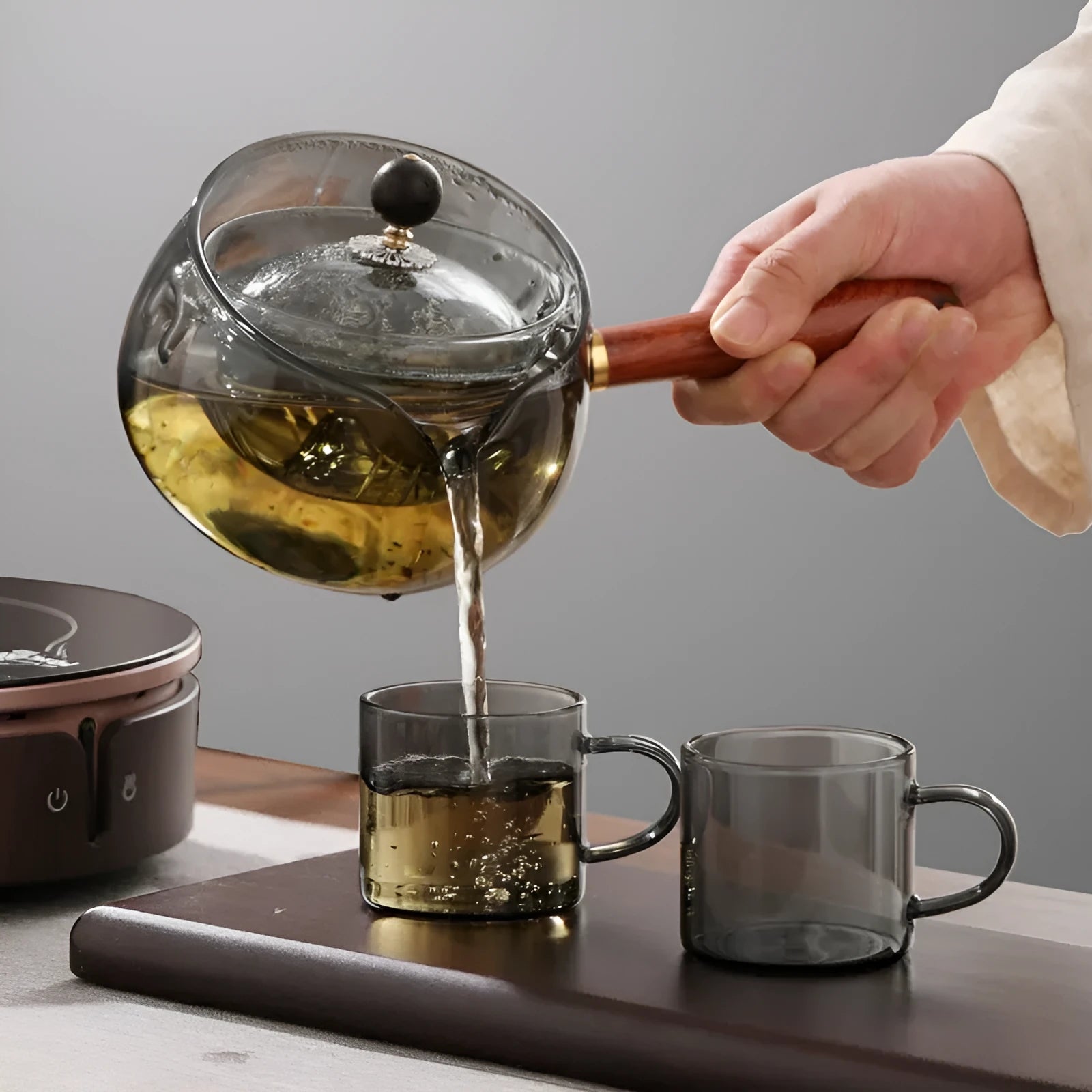Grey and transparent rotary glass teapot with wooden handle and infuser on a kitchen counter