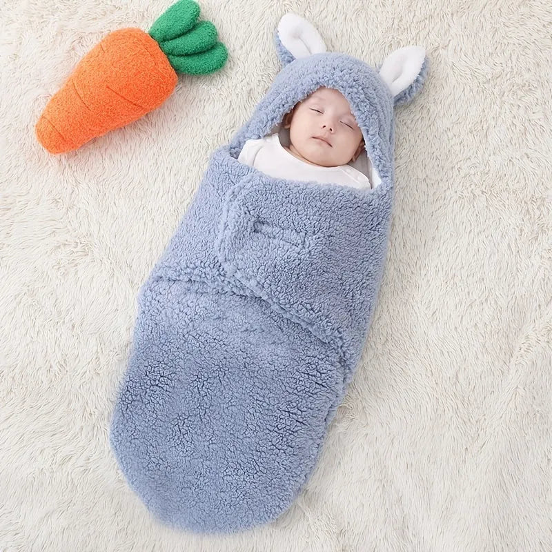 Baby wearing a blue adjustable cotton sleep sack with velcro swaddle closures and a head-protecting hood.