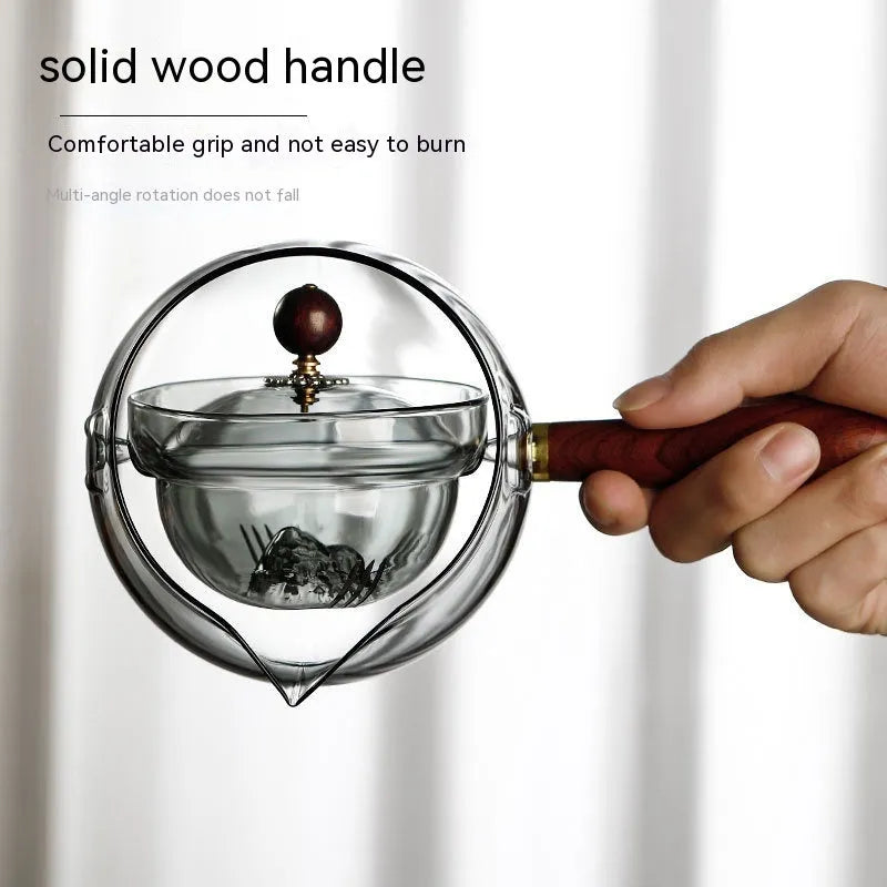 Grey and transparent rotary glass teapot with wooden handle and infuser on a kitchen counter