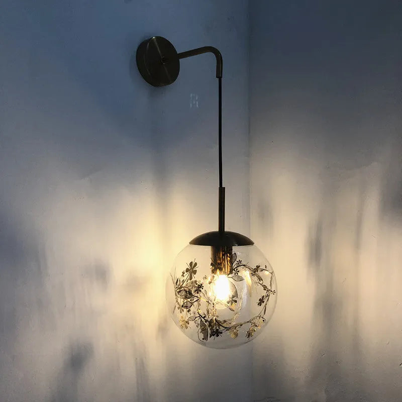 Modern small glass wall lamp in golden flower finish mounted on a bedroom wall.