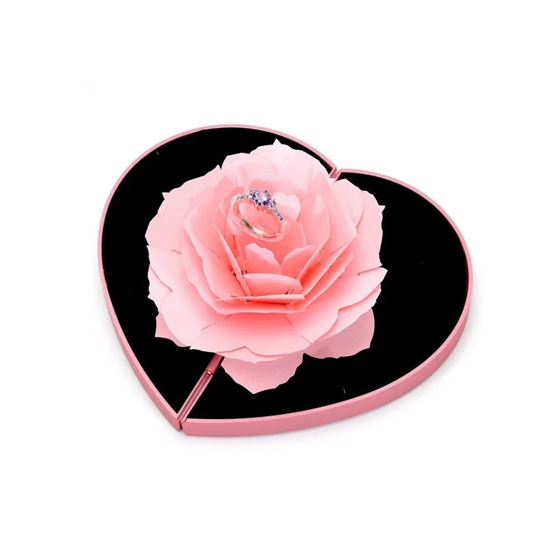 Red heart-shaped rotating ring box with 3D white rose decoration on top.