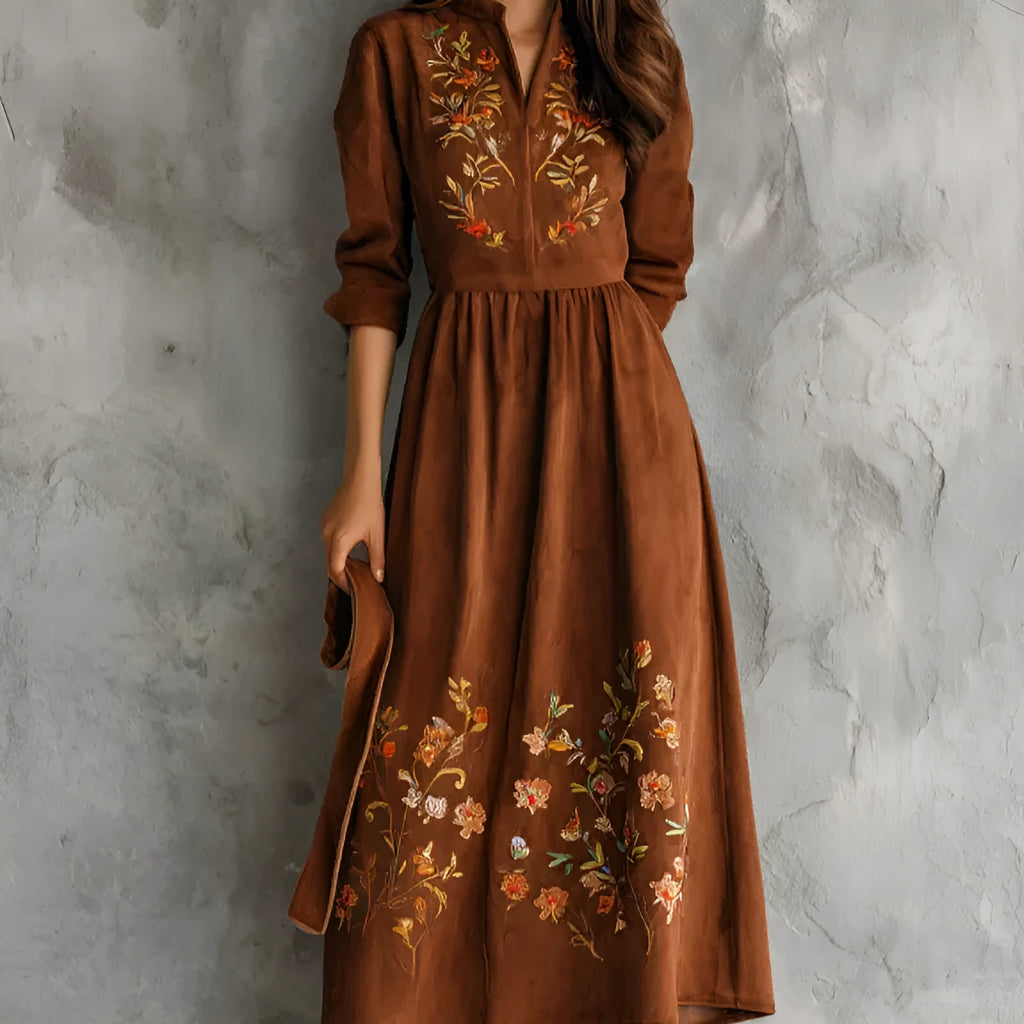 Brown suede-look midi dress with detailed floral embroidery on the bodice and hem, featuring three-quarter sleeves.