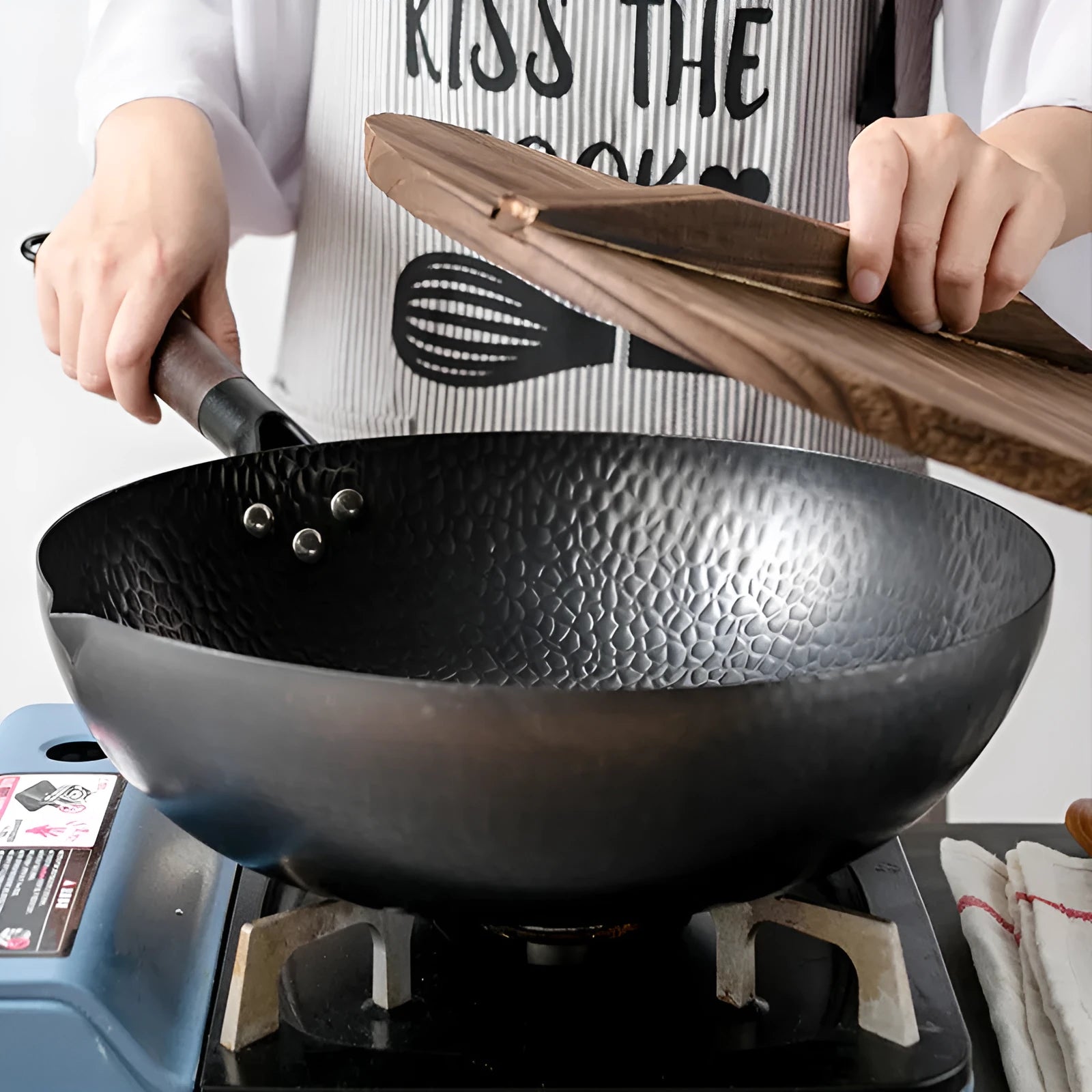Handmade black iron wok pan with a long wooden handle on a kitchen counter.