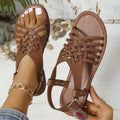 Flat buckle open toe Roman style cross strap sandals in black on a beige background.