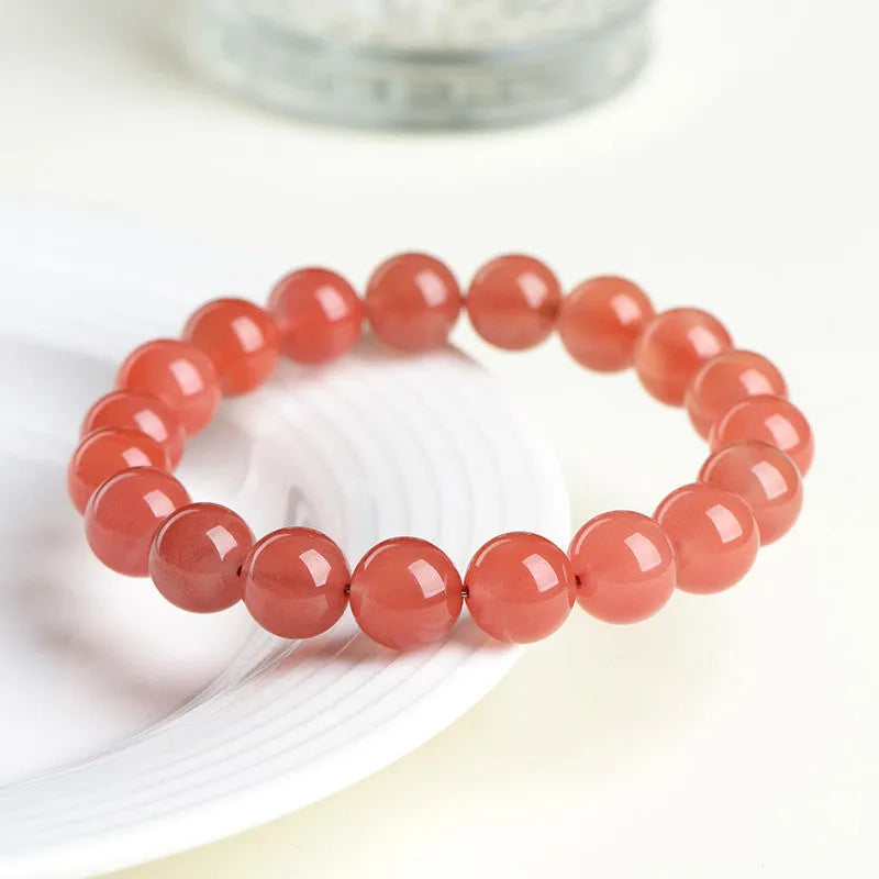 Natural cherry red agate bracelet with hand-polished beads on a wrist, showing colour variation and secure clasp.