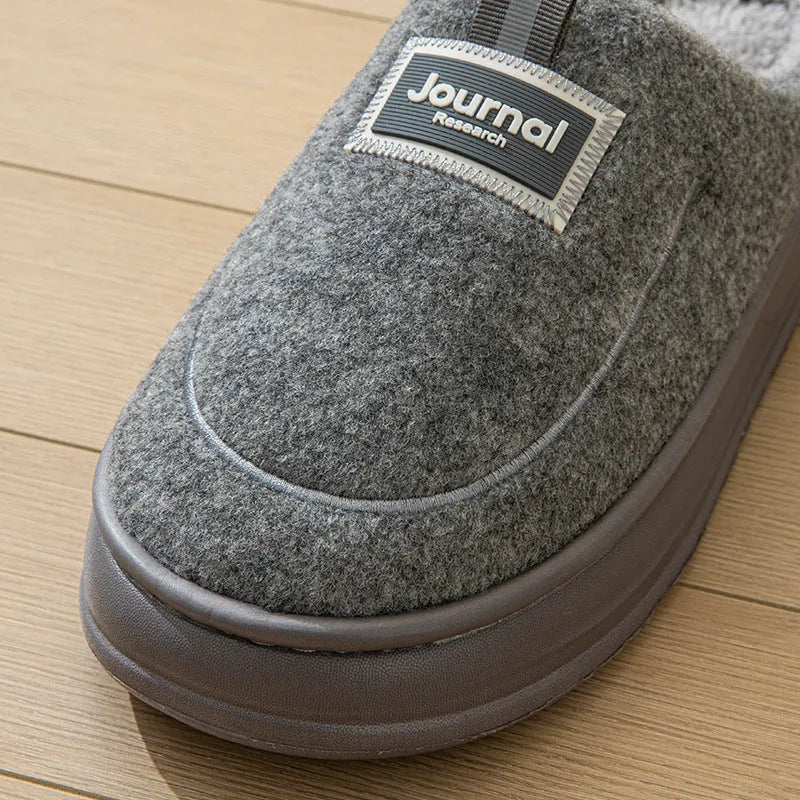 Men's brown suede slippers with a thick, textured sole on a wooden floor
