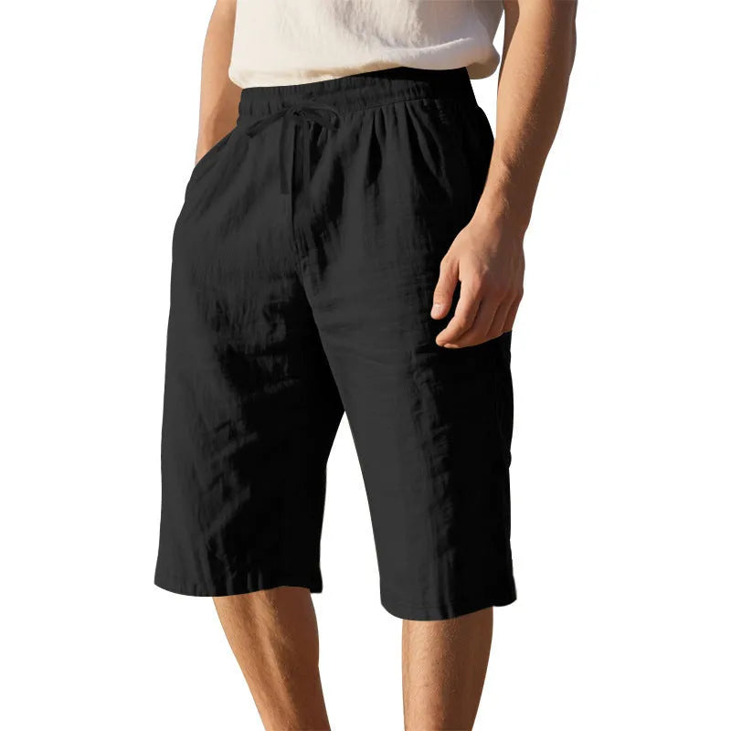 Man wearing loose-fit, solid-colour linen shorts in a light blue shade, showing the cropped length and drawstring waist.