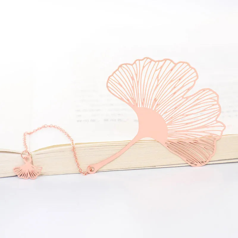 Detailed brass bookmark with hollow maple leaf pendant and rose gold tassel on a book page.
