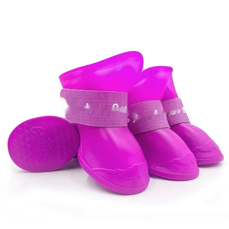 Set of four colourful rubber dog rain shoes with anti-slip soles on a wet surface.