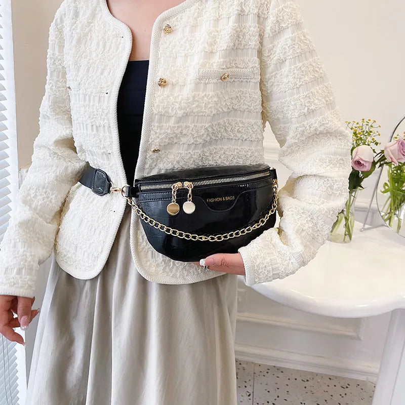 Shiny hard-shell PU chest bag with wide shoulder strap, chain detail, and internal pockets in silver colour