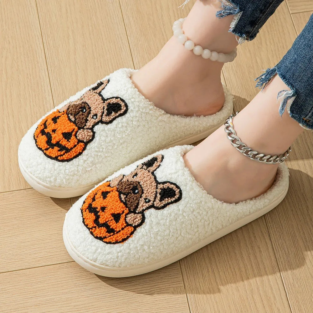 Black and white plush Halloween pumpkin slippers with textured rubber soles on a wooden floor.