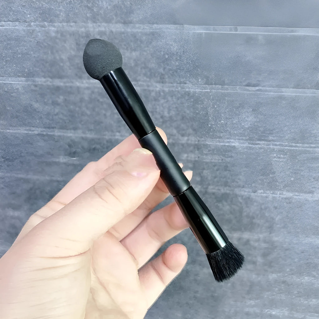 Black wooden handle concealer brush with a grey sponge tip applicator angled for under eye use.