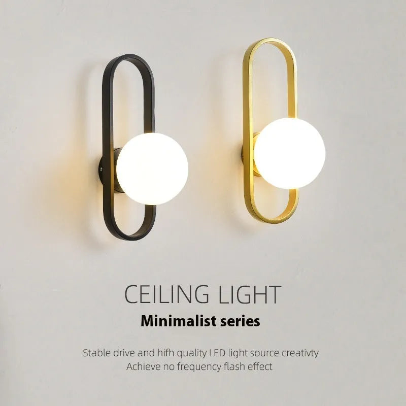 Modern minimalist wall lamp with black iron arm and clear glass shade, mounted on a plain wall.