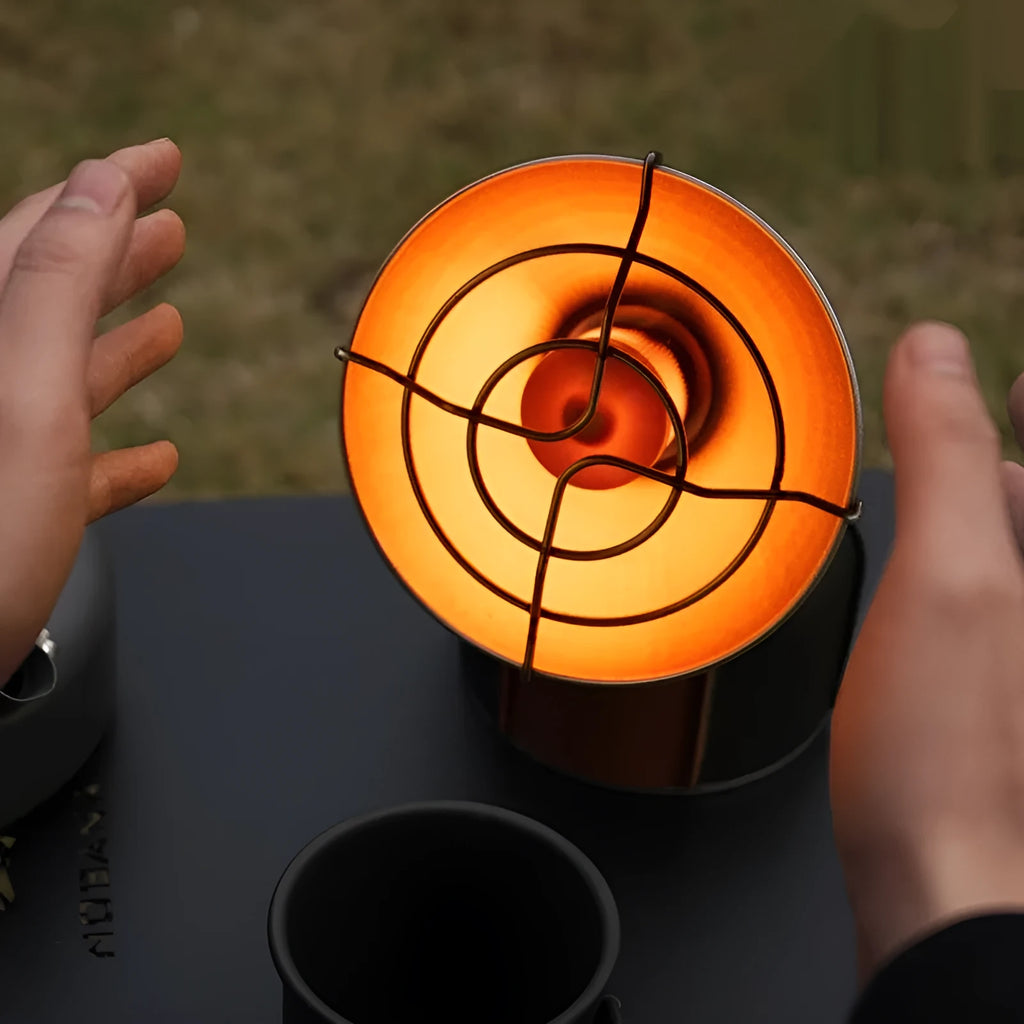 Black and orange portable camping heater stove with automatic ignition on a rocky outdoor surface.
