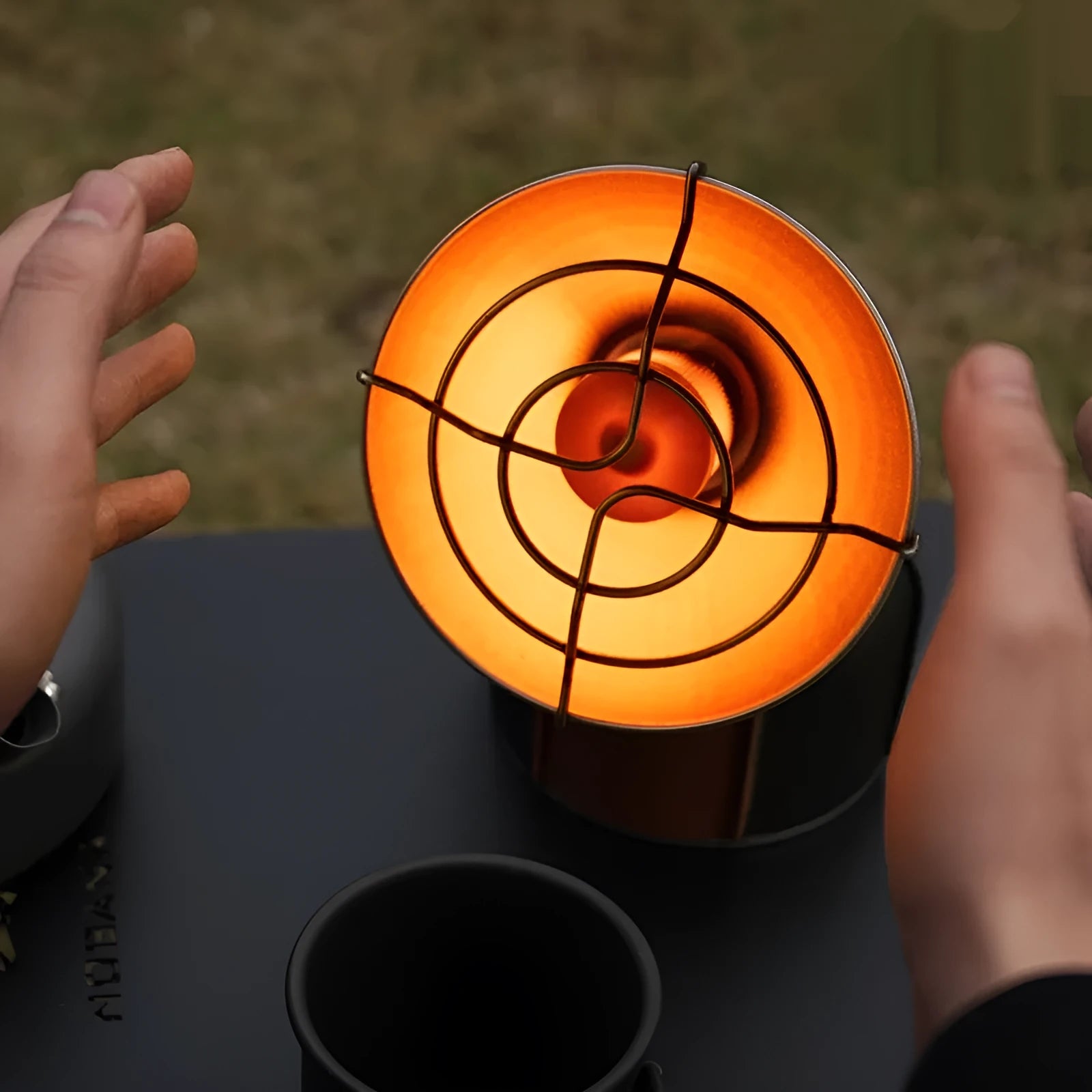 Black and orange portable camping heater stove with automatic ignition on a rocky outdoor surface.