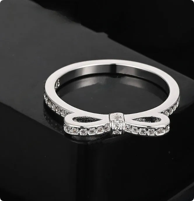 Silver coloured bow-shaped ring with sparkling rhinestone crystals on a model's hand.