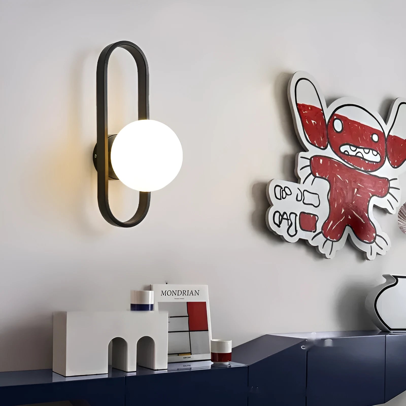 Modern minimalist wall lamp with black iron arm and clear glass shade, mounted on a plain wall.