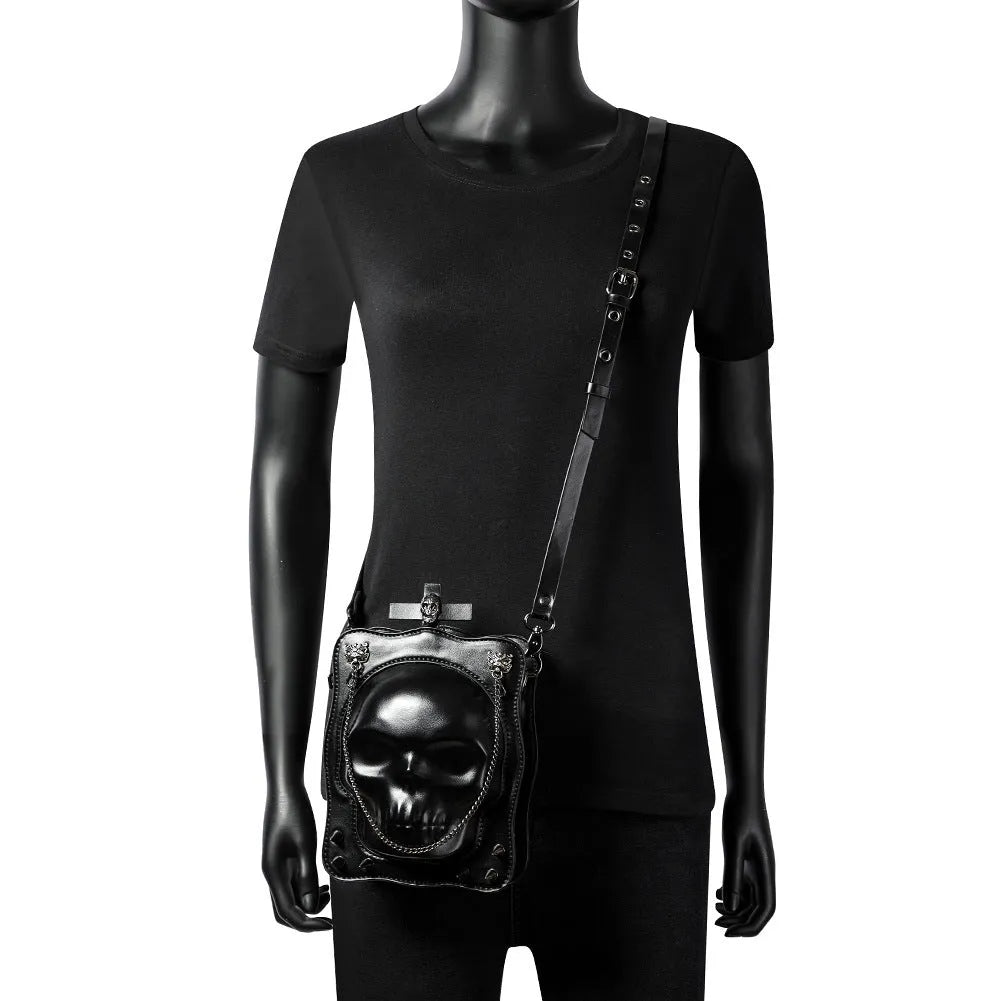 Black mini square crossbody bag with embossed skull design, metal chain strap, and zip closure.