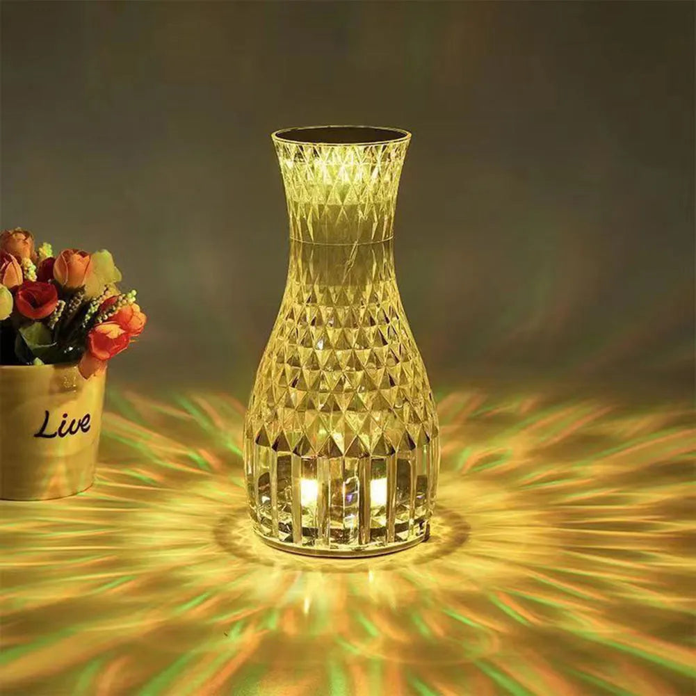 Vase-shaped transparent crystal bedside lamp with touch controls and LED lights on a table.