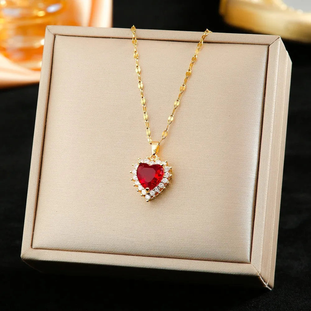 Gold red titanium steel necklace with heart and flower pendant, matching stud earrings, and ring on a grey background.