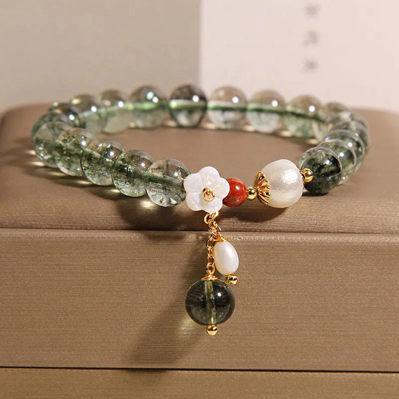 Women's green phantom quartz crystal bracelet with small shell flower accent on wrist.