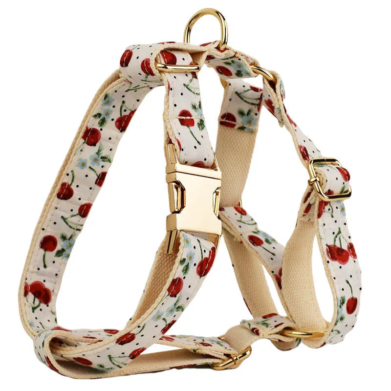 Red cherry print pet collar, lead, and harness set with light gold buckles and matching waste bag dispenser