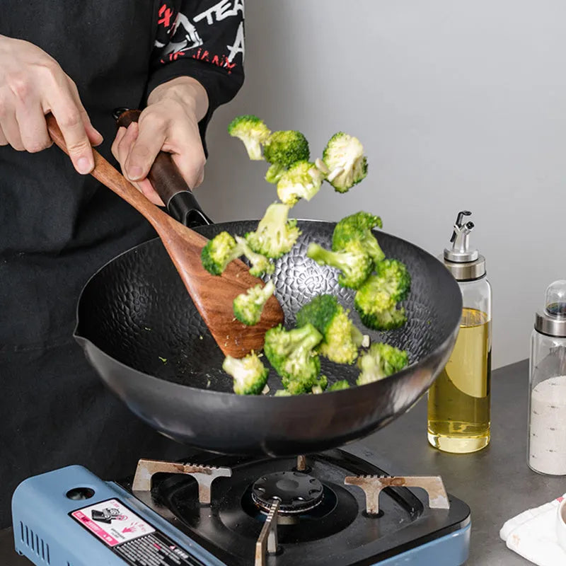 Handmade black iron wok pan with a long wooden handle on a kitchen counter.