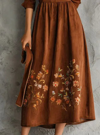 Brown suede-look midi dress with detailed floral embroidery on the bodice and hem, featuring three-quarter sleeves.