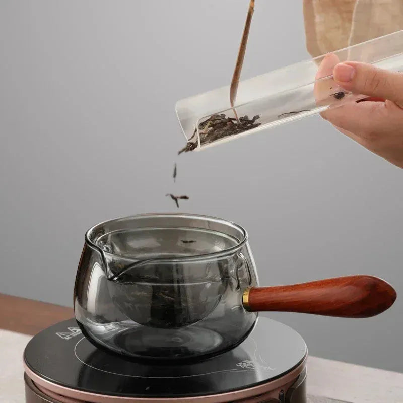 Grey and transparent rotary glass teapot with wooden handle and infuser on a kitchen counter