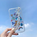 White TPU iPhone case with an attached silver bear pendant on a chain, showing cartoon-style design.