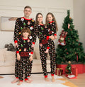 Family wearing matching Christmas pyjamas with plaid and cartoon prints, including adults, children and a dog in coordinated sleepwear