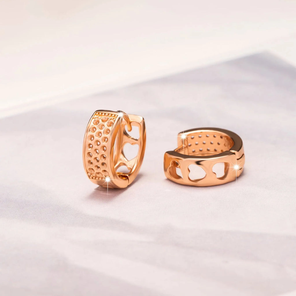 Close-up of a pair of rose gold circular hoop earrings with three small hollow heart shapes cut out of each band.