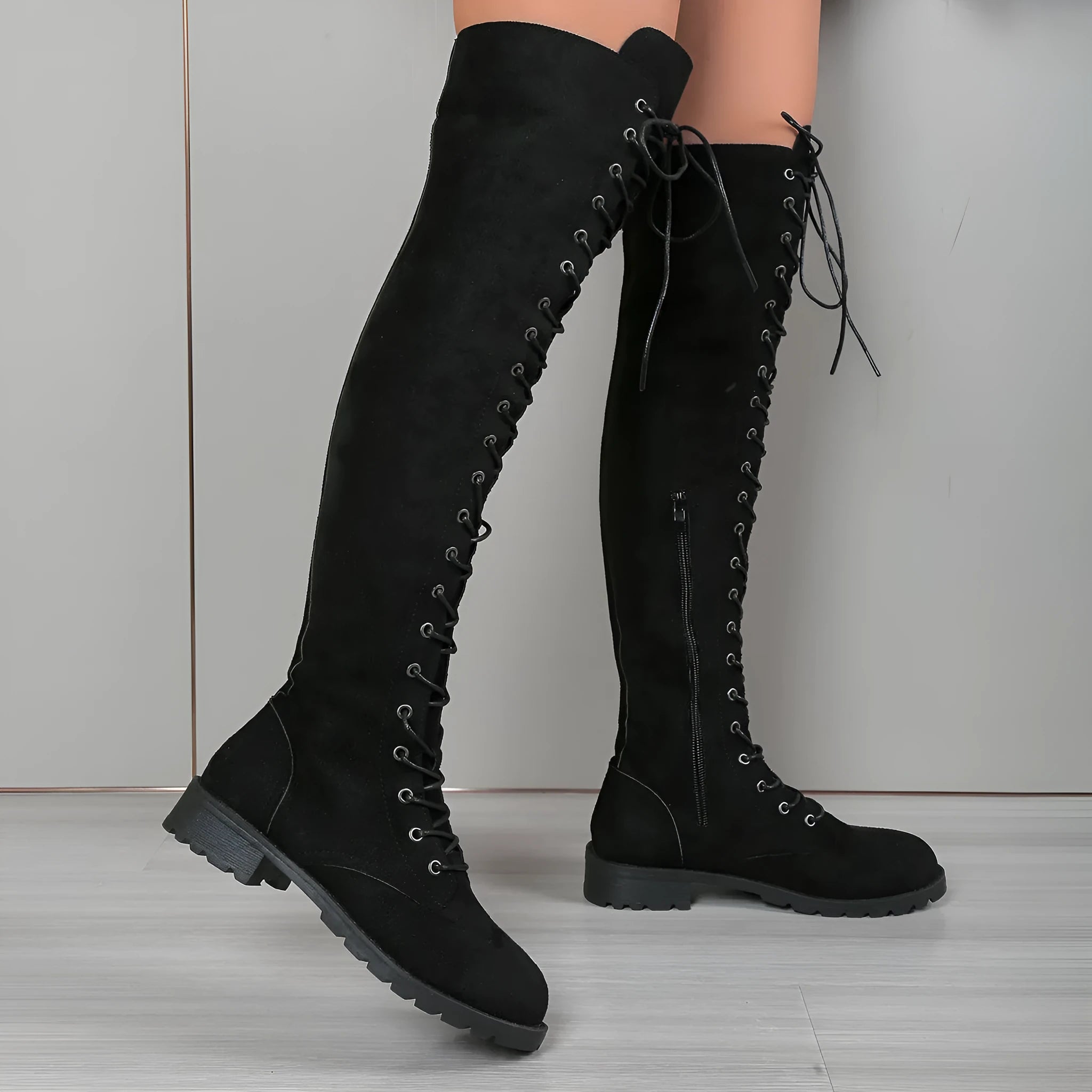 Black lace-up over-the-knee boots with a round toe and flat rubber sole on a neutral background.