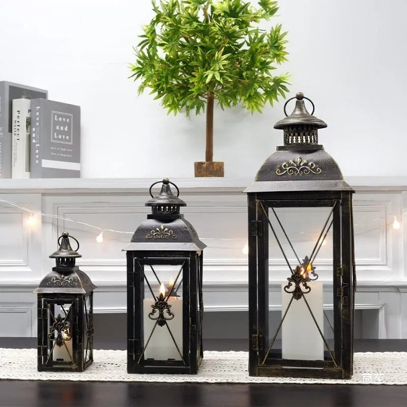 Black wrought iron floor-standing storm lantern with clear tempered glass panels on a garden patio.