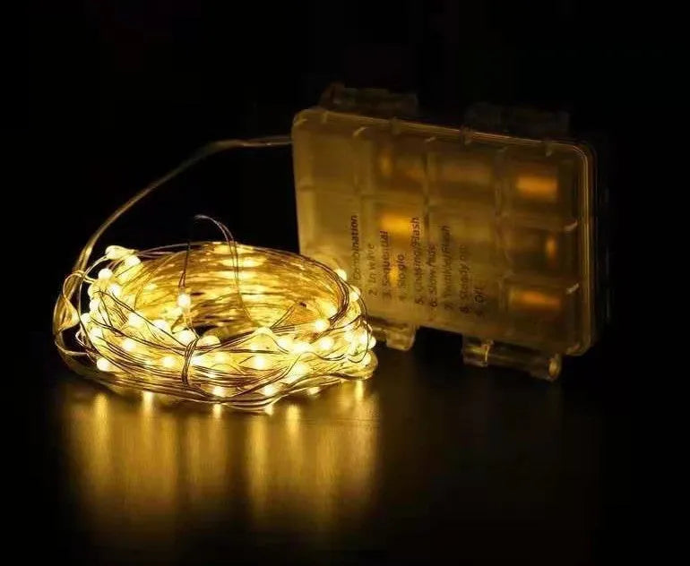 Close-up of flexible copper wire string light with 120 tiny LED bulbs, shaped in a spiral next to the battery control box.
