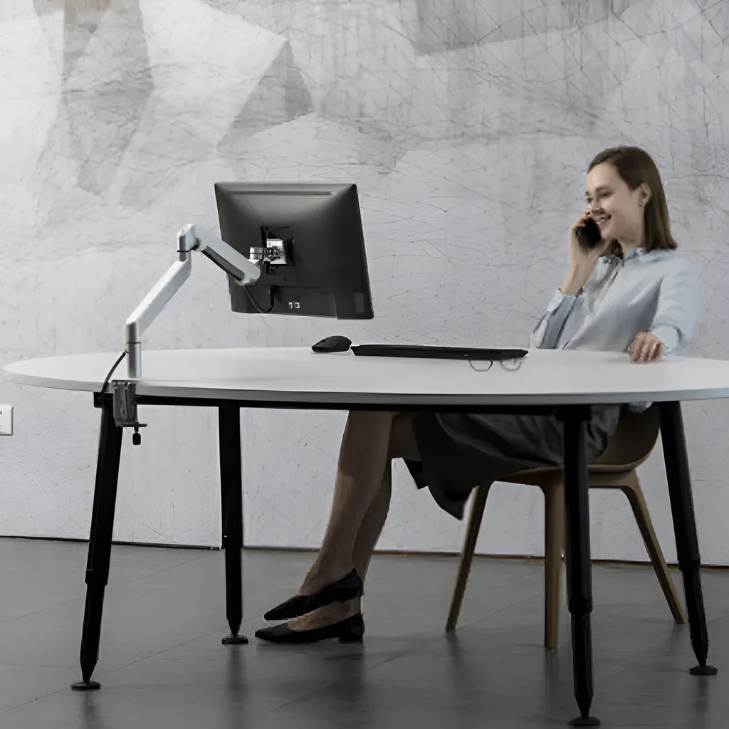 Silver aluminium laptop stand with an adjustable arm bracket on a wooden desk.
