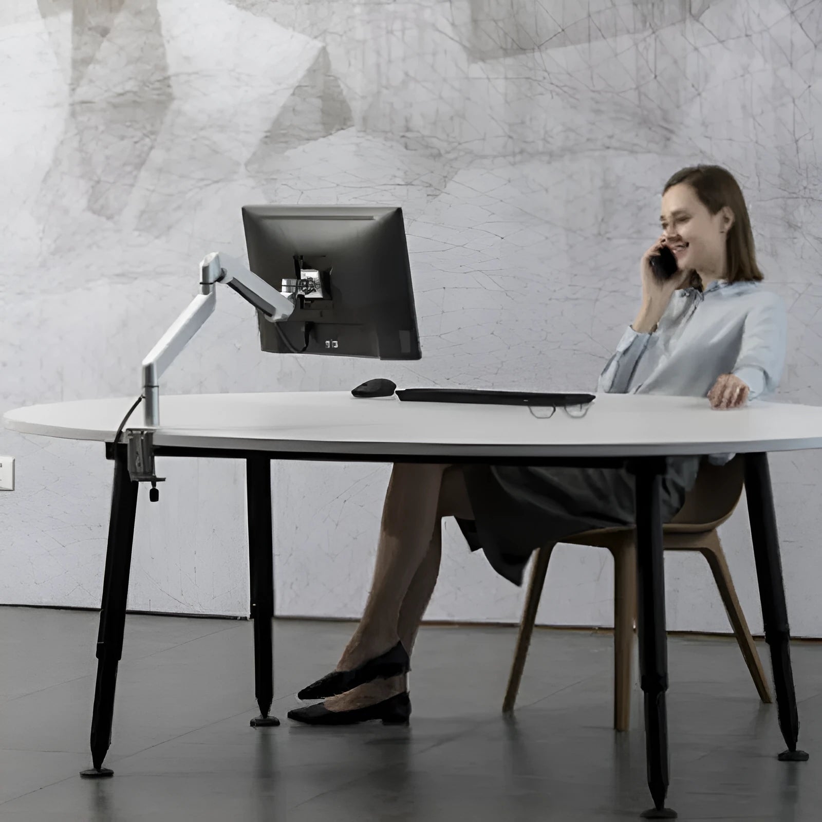 Silver aluminium laptop stand with an adjustable arm bracket on a wooden desk.