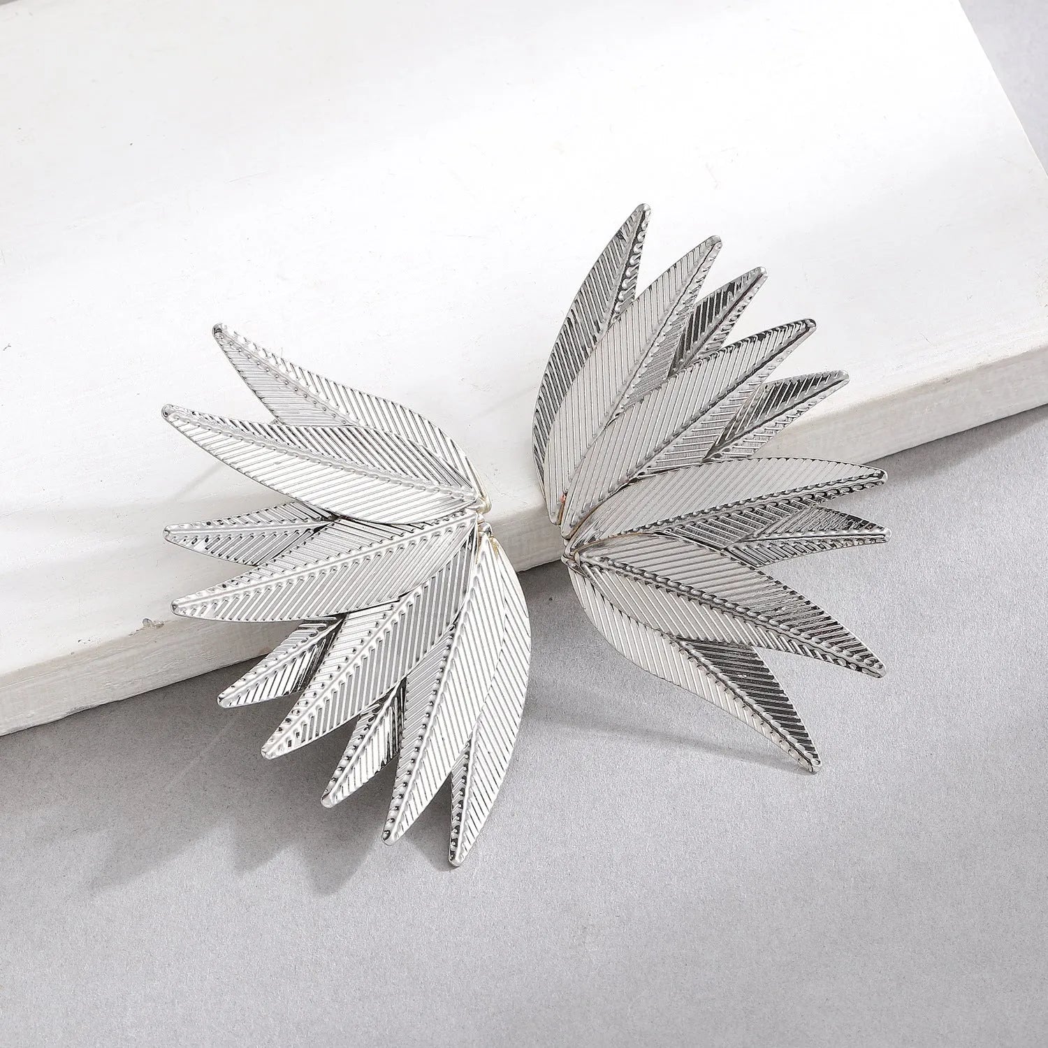 A pair of gold or white alloy earrings shaped like a leaf.