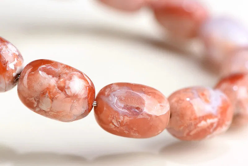 Natural cherry agate barrel bead bracelet with Ruyi charm on a wrist.