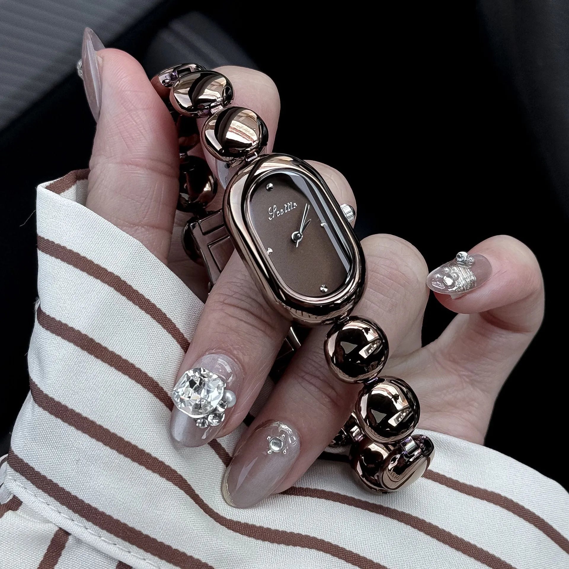 Oval women's fashion watch on wrist showing 9mm thick case, available in black gold, platinum and other colours.